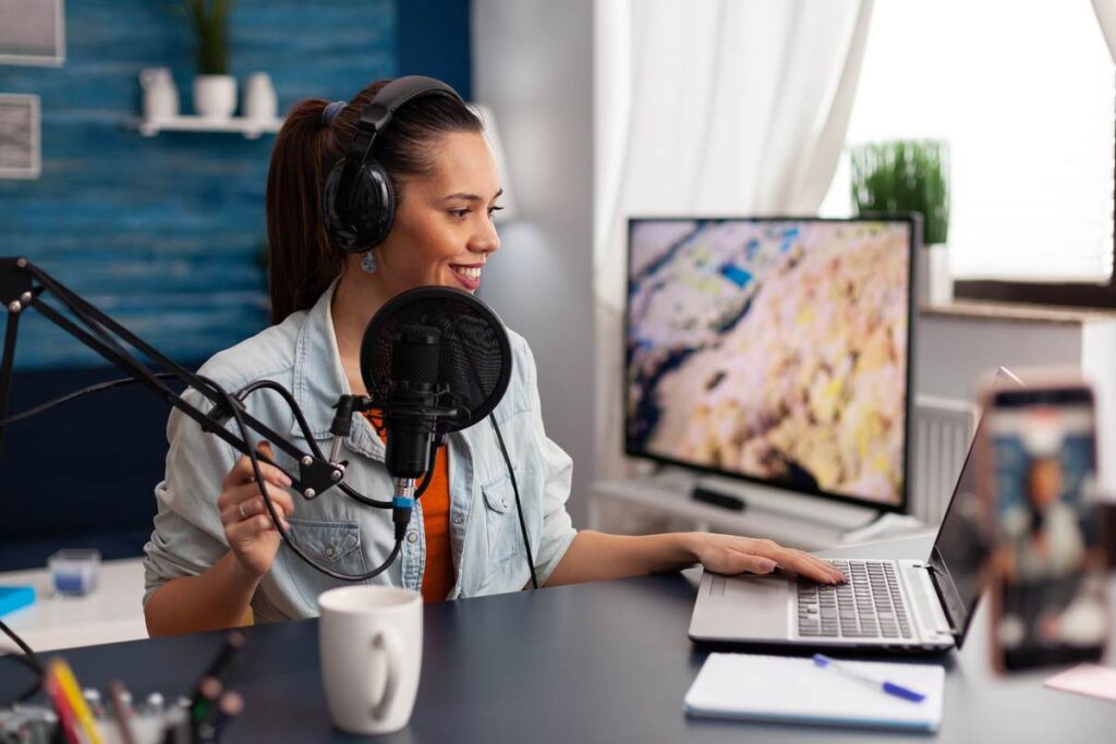 Produtora gravando podcast e ajustando no editor de áudio no laptop.