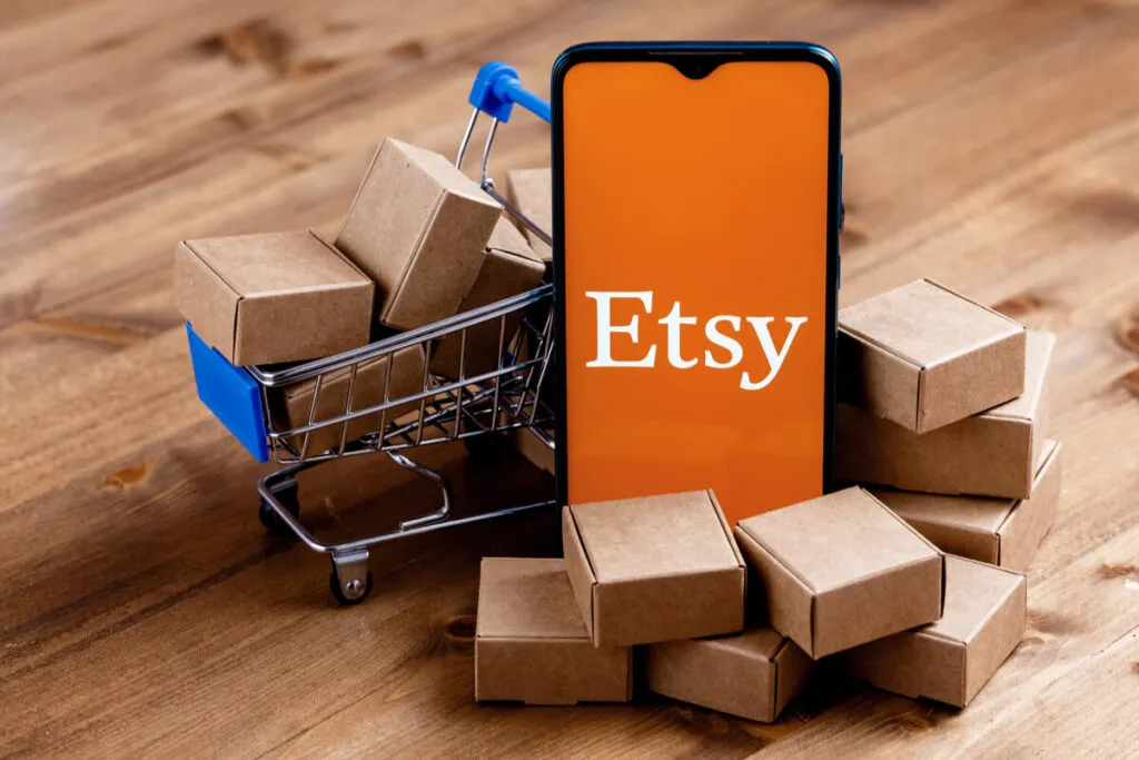 Um celular com o logo da Etsy ao lado de uma miniatura de carrinho de compras