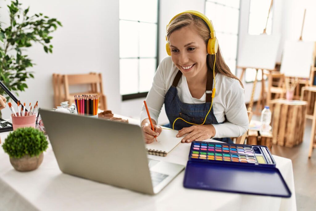 Uma mulher desenhando em frente a um computador, usando fones de ouvido e sorrindo