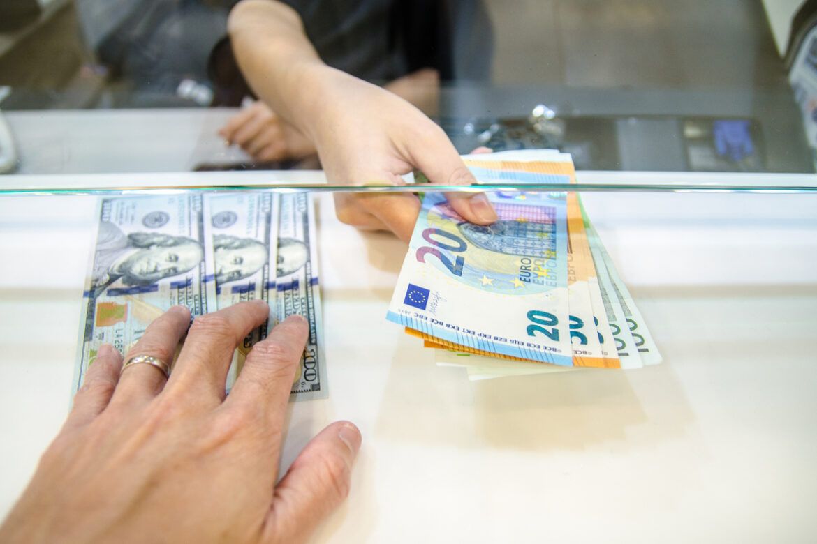 Foto das mãos de duas pessoas trocando notas de dólar por notas de euro