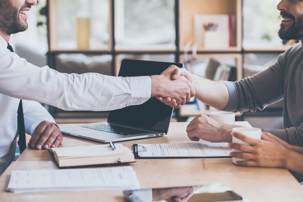 Dois homens brancos em um aperto de mão, simulando como fazer upsell.