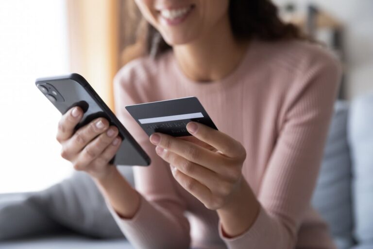 Mulher sorrindo olhando para o telefone e um cartão de crédito