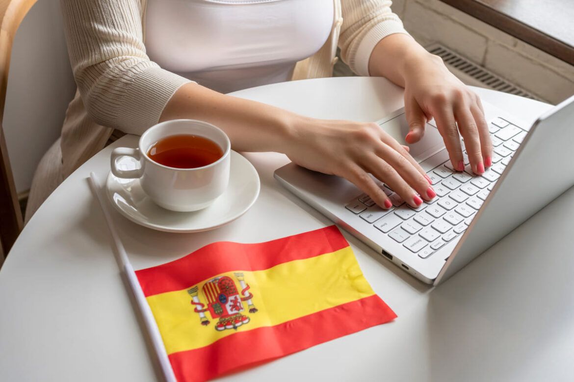 Mulher mexendo no computador com uma bandeira da Espanha do lado