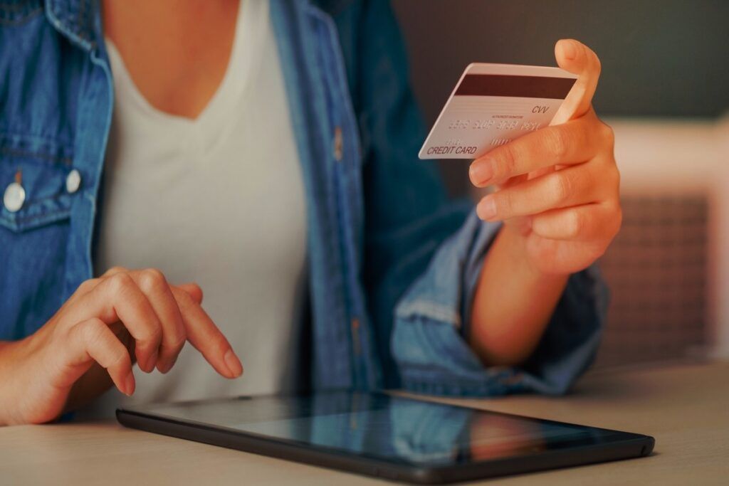 Mulher segurando cartão de crédito e acessando o tablet