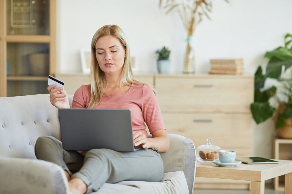 Mulher sentada no sofá com celular na mão e computador no colo