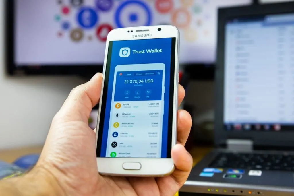 Close-up de mão segurando o smartphone com a tela do app da Trust Wallet