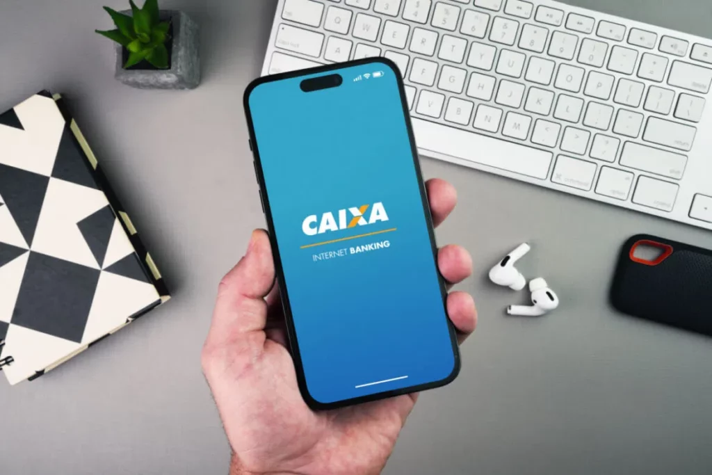 Imagem de uma mão segurando o celular com a tela de abertura do aplicativo da Caixa Econômica Federal