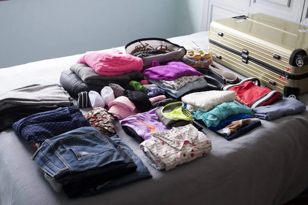 Várias roupas dispostas em uma cama ao lado de uma mala de viagem
