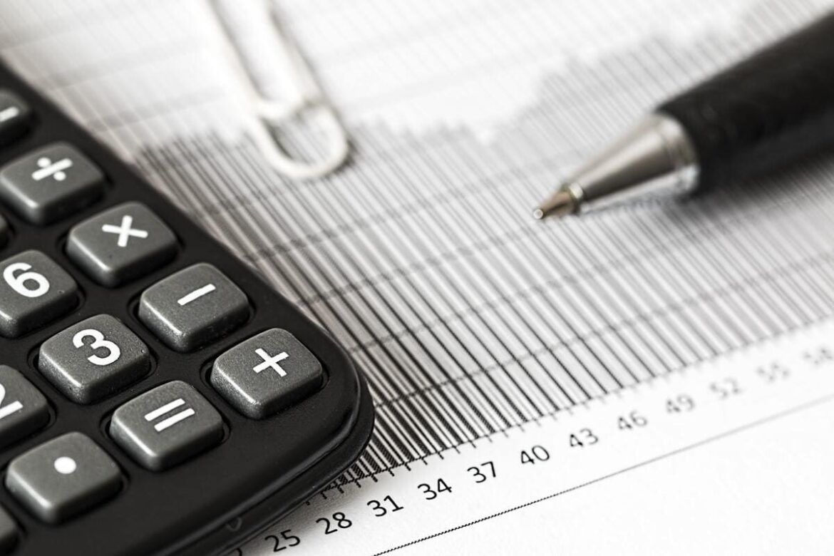 Calculadora, caneta e clips em cima de um papel fazendo o calculo do IVA.