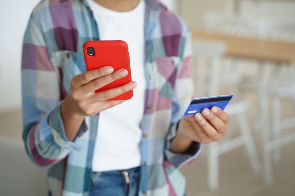 Mulher com smartphone na mão e cartão de crédito.