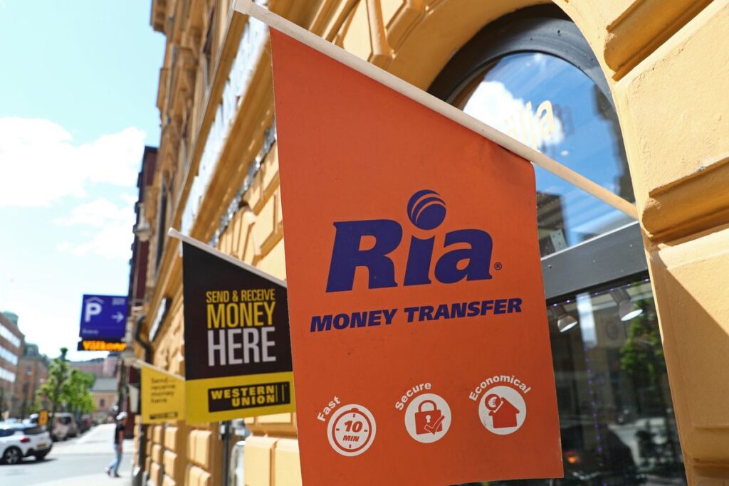 Banner com logo da Ria Money Transfer em uma agência da empresa.