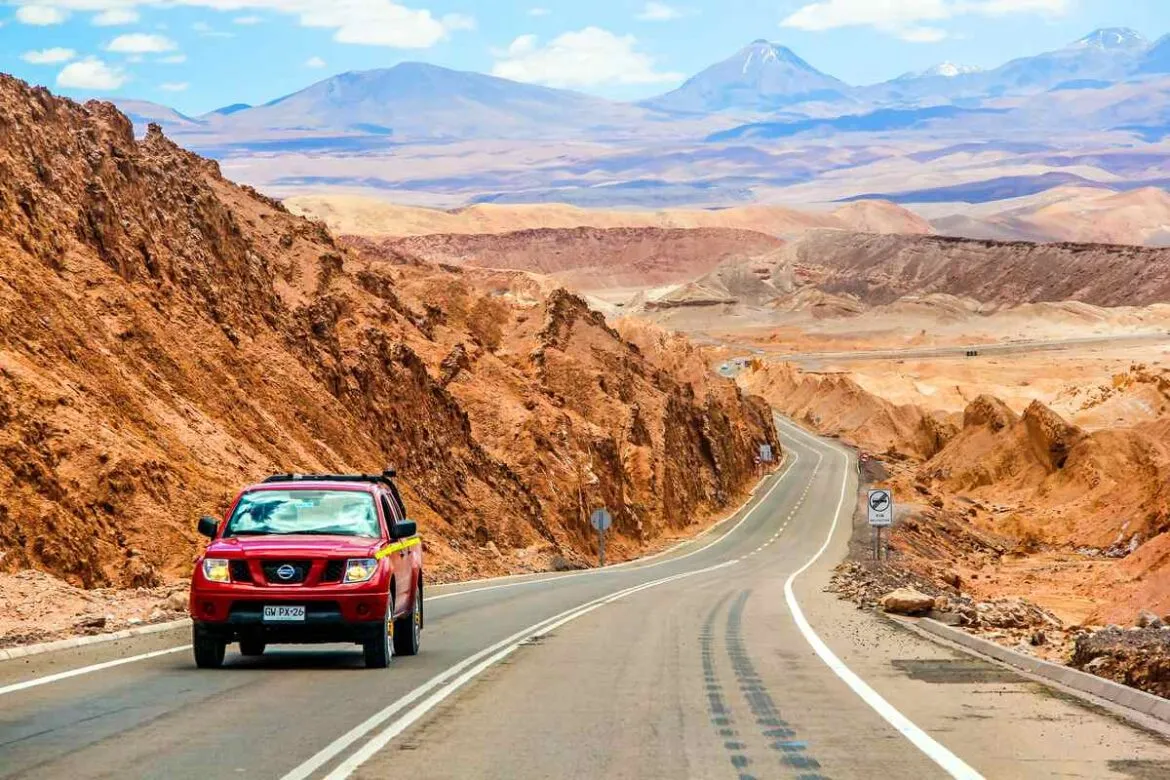 Carro vermelho viajando por uma estrada no deserto chileno.