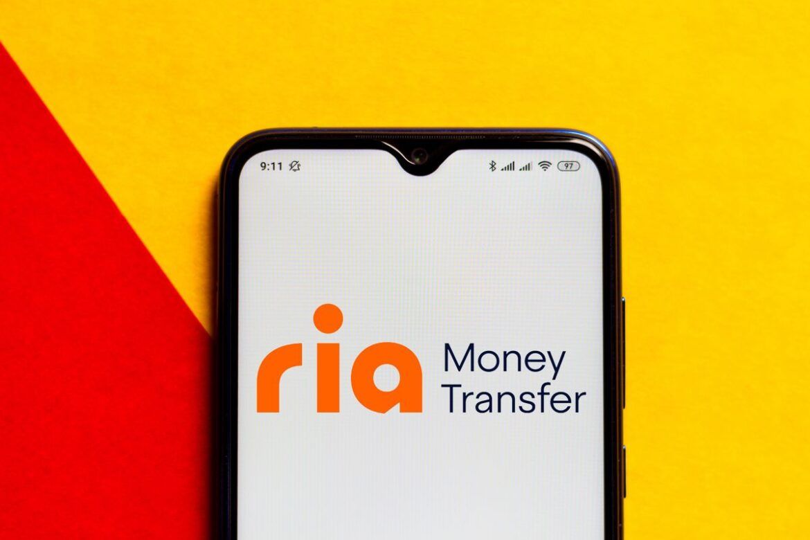 Smartphone com o logo da Ria Money Transfer na tela.