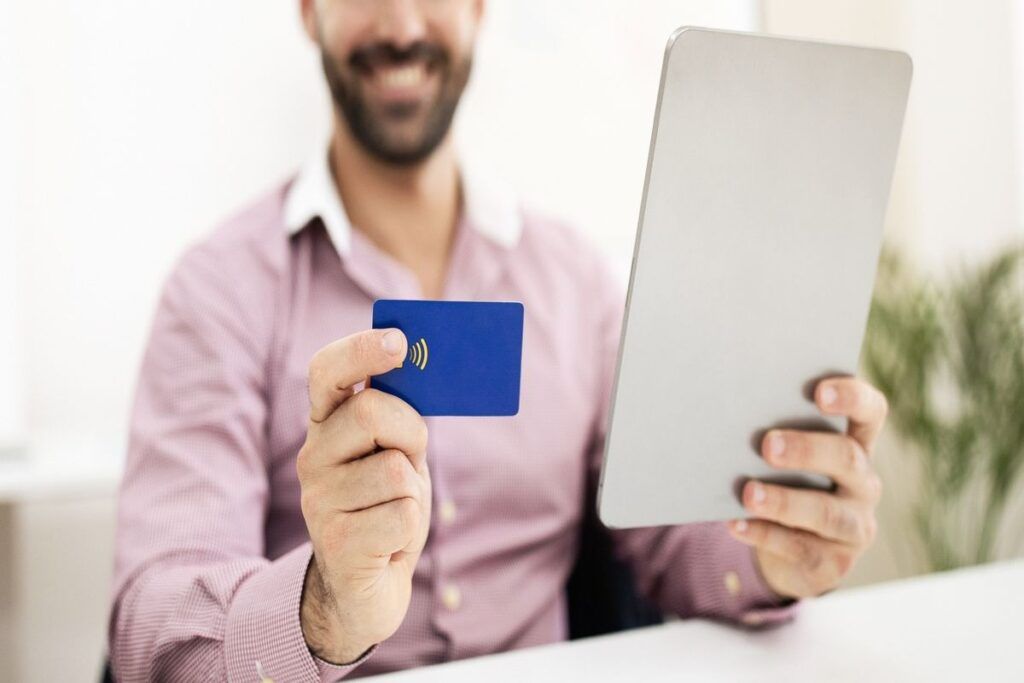 Homem sorrindo enquanto segura cartão de crédito e tablet. 
