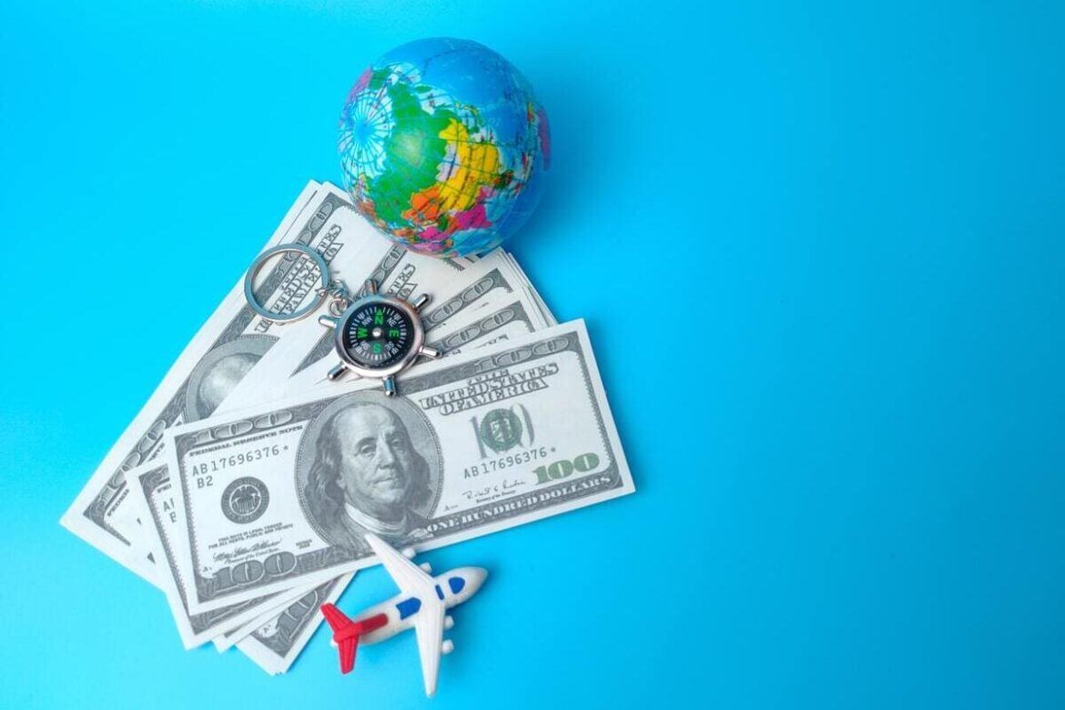 Dólares, um globo do planeta Terra e um avião em miniatura em cima de um fundo azul, representando a possibilidade de transferir o patrimônio para o exterior.