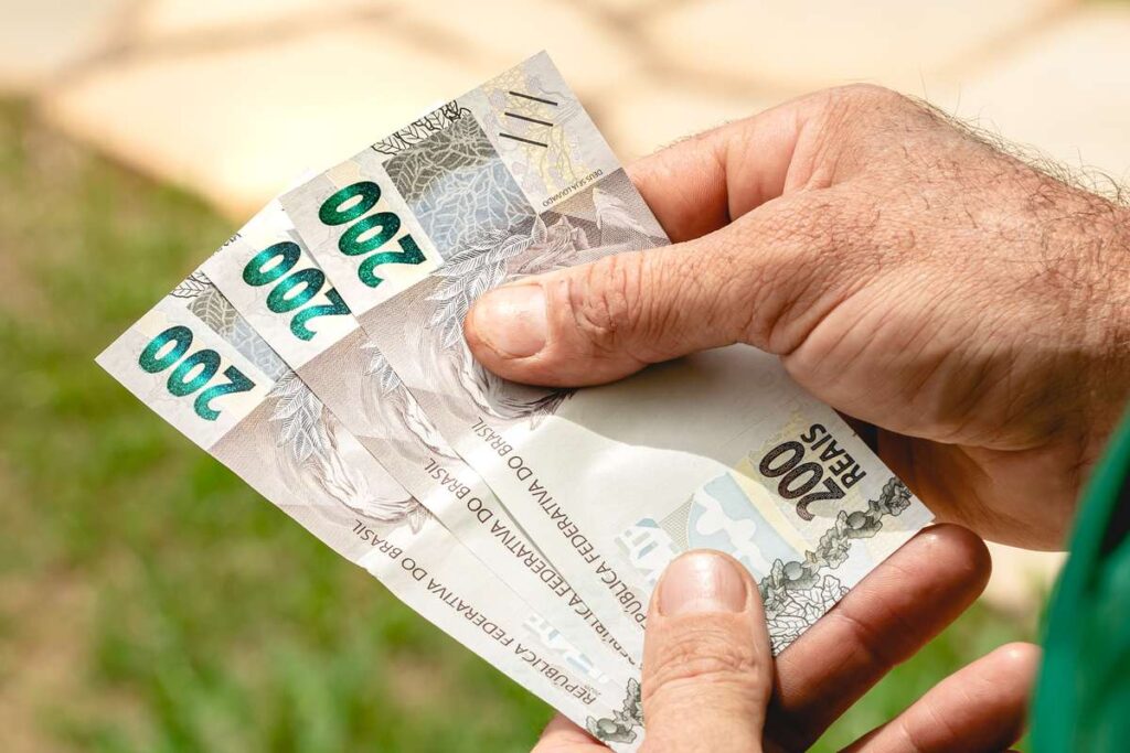 Homem segurando três notas de 200 reais.