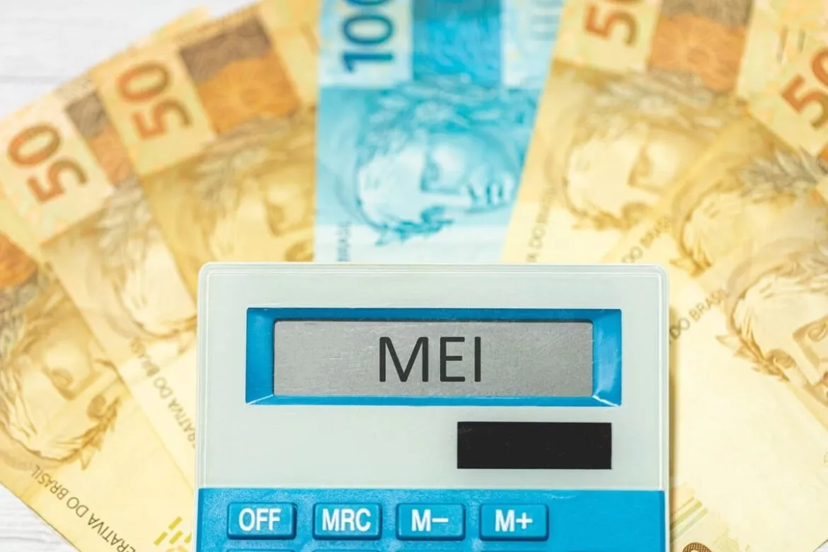 A imagem possui uma calculadora escrito "MEI" em destaque, com notas de dinheiro atrás, simbolizando compensação monetária recebida e paga.