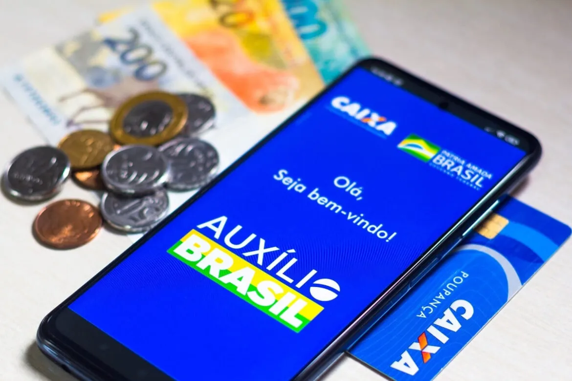 Nesta ilustração, o logotipo do Auxílio Brasil está exibido em um smartphone, ao lado de notas de dinheiro real brasileiro, para ilustrar a indenização Auxílio Brasil.