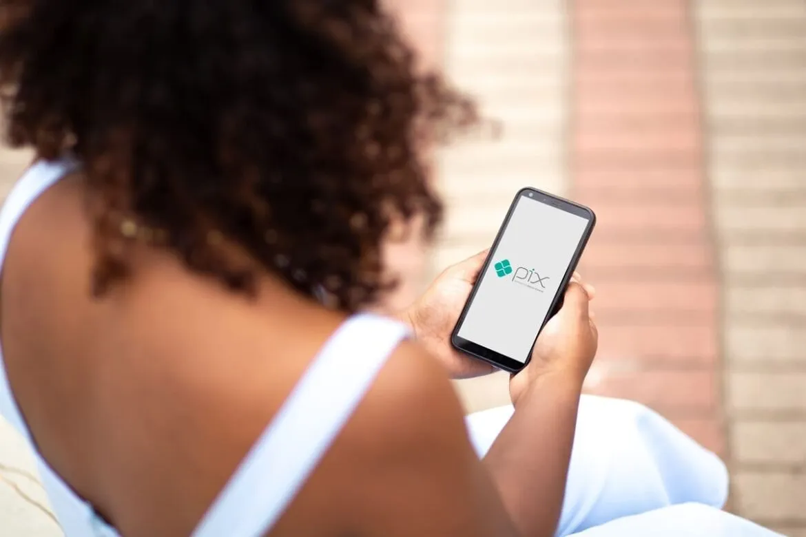 A imagem retrata uma mulher negra vista de cima, segurando um telefone e abrindo a plataforma do PIX na função cartão de crédito.