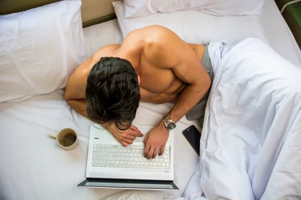 Homem deitado na cama acessando sua conta da 2Close pelo notebook. 