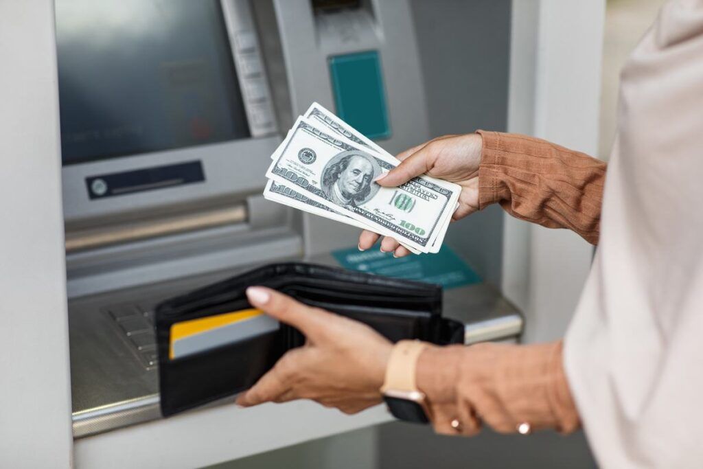 Mulher guardando dólares na carteira após sacar dinheiro do caixa eletrônico. 