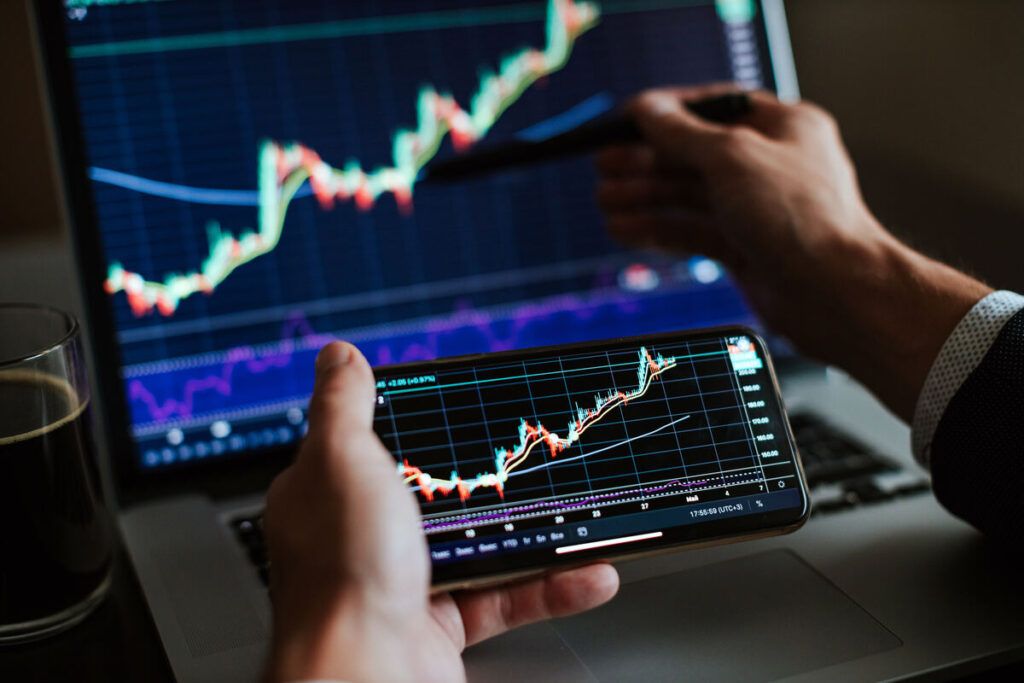 Tela de computador e celular com trading de investimentos