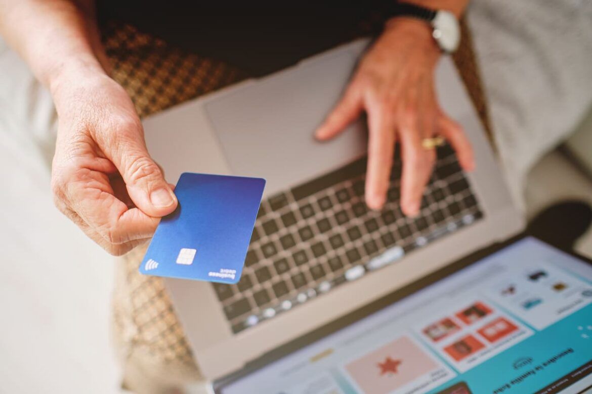 Pessoa segurando um cartão de crédito em frente ao computador para ilustrar um texto sobre uma fraude feita em nome do Nox Bank