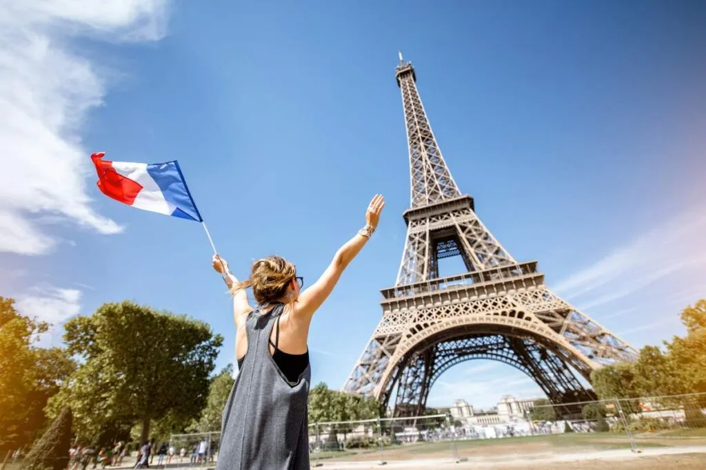 Mulher segurando a bandeira da França e admirando a Torre Eiffel. 