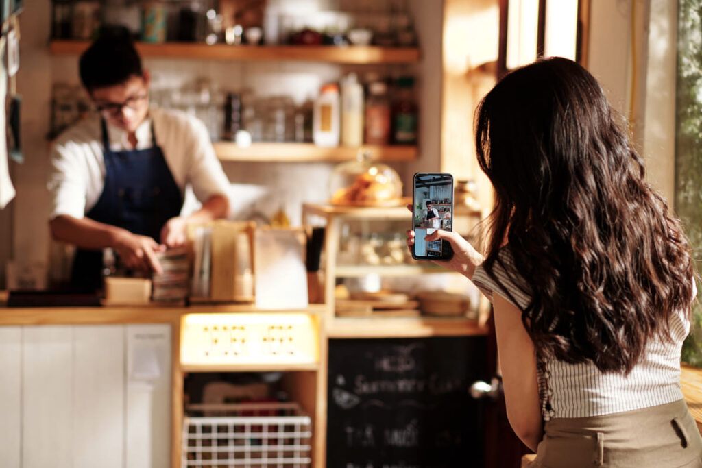 Mulher filmando com um celular na mão, trabalhadora de cafeteria.