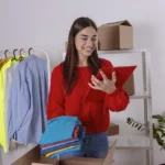 Mulher sorridente organizando roupas e verificando uma prancheta em seu estoque, ilustrando o guia de como vender na Shein sem estoque.
