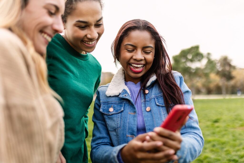 Mulheres sorrindo enquanto visualizam fotos nas redes sociais.
