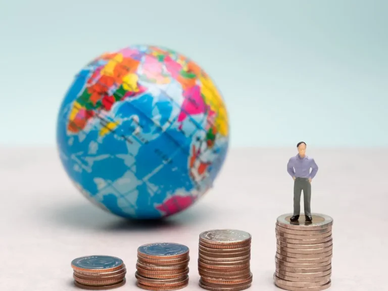 Miniatura de homem sobre pilhas de moedas com um globo terrestre ao fundo, ilustrando o guia de como declarar investimentos no exterior.