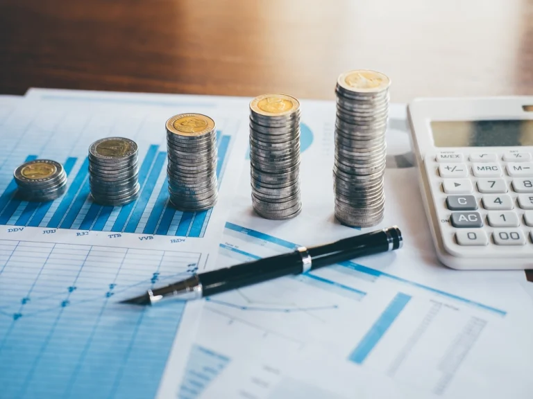 Pilhas de moedas crescentes sobre gráficos financeiros com caneta e calculadora, auxiliando na escolha entre declaração completa ou simplificada.