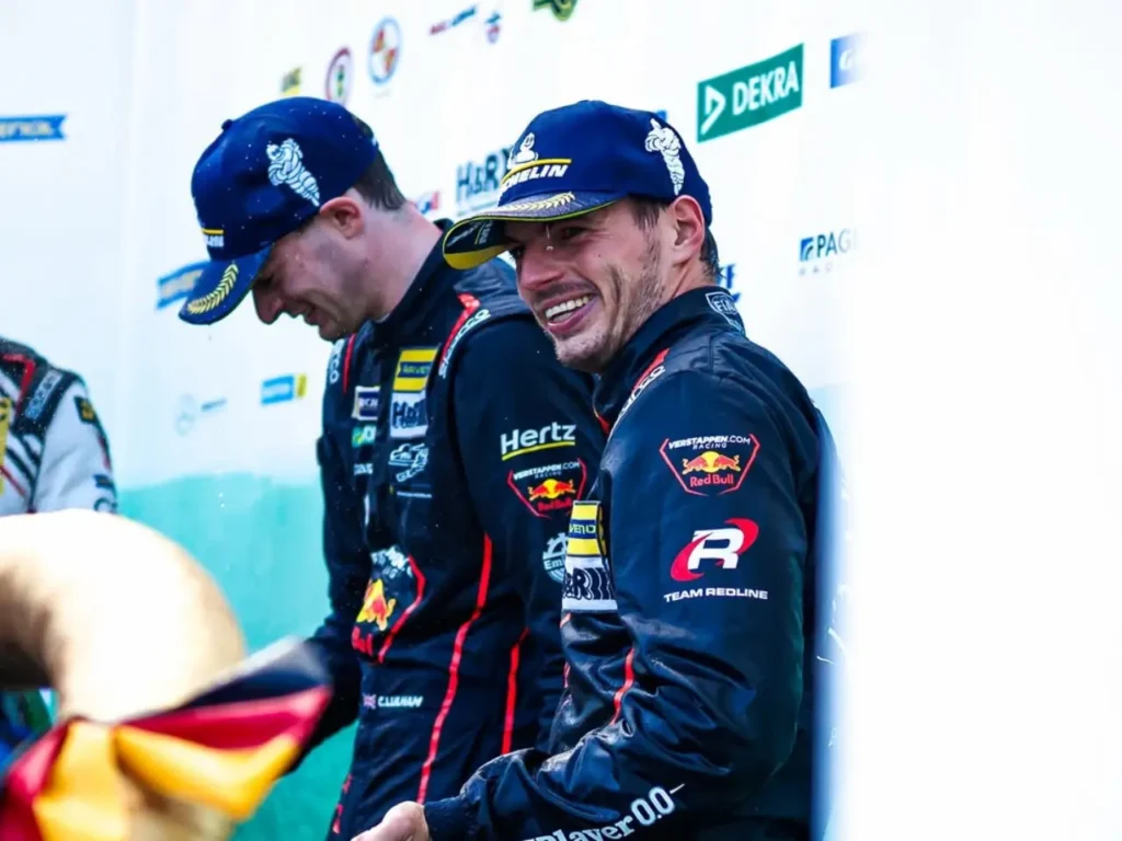 Max Verstappen sorrindo no pódio da NLS, usando boné e macacão de corrida com logos da Red Bull e Verstappen Racing.