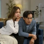 Casal jovem assiste à TV no sofá com expressão de expectativa, representando a emoção de acompanhar um dorama novo em casa.
