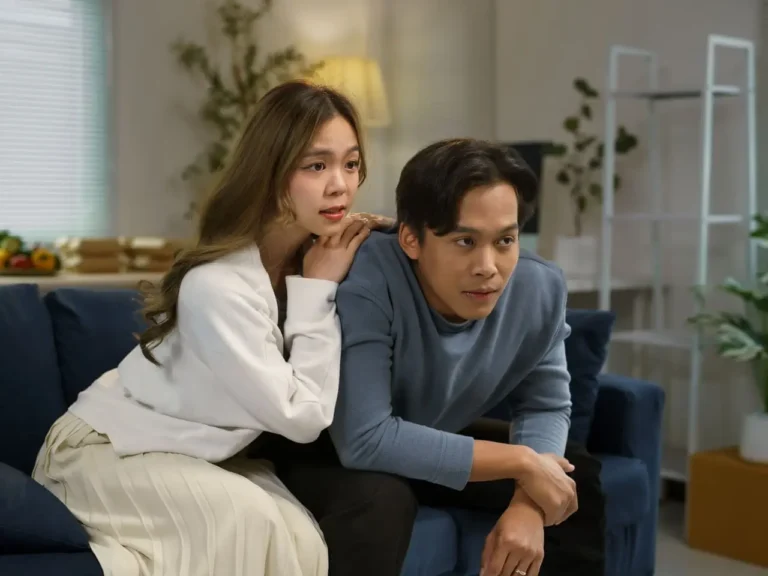 Casal jovem assiste à TV no sofá com expressão de expectativa, representando a emoção de acompanhar um dorama novo em casa.