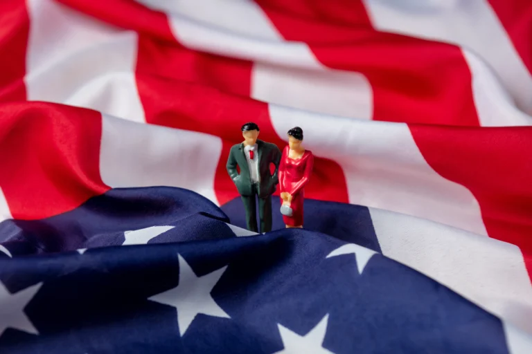 Miniaturas de um casal sobre a bandeira americana ondulada, ilustrando o contexto histórico de quem descobriu os Estados Unidos.