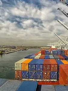 Navio carregado com contêineres próximo aos guindastes de um terminal portuário.
